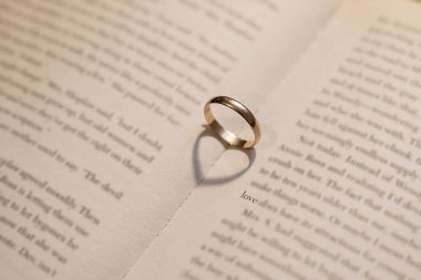 Aşk işareti olarak alyans. Evlilik yüzüğü açık bir kitapta aşk kelimesinin yanında. Yüzüğün kalp şeklinde bir gölgesi var. Bir aşk ilanı.