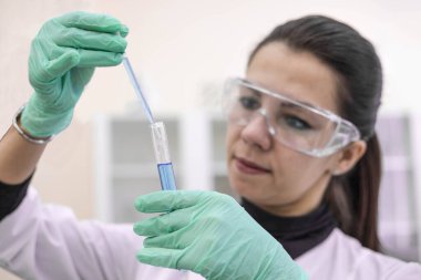 Laboratuvarda bir kadın bilim adamı test tüpündeki aşıyı inceliyor. Laboratuvarda bir aşı üretiyor..