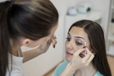 Usta, kaş arasındaki destek hatlarını pamuklu çubukla düzeltiyor. Bir kaş çizimi yap. Kalıcı makyaj. Kaşların düzeltilmesi ve renklendirilmesi.