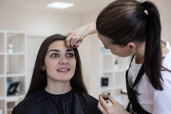 A beautiful happy brunette does henna eyebrow coloring in a beauty salon. The concept of correction and coloring of eyebrows with henna. Self-care, beauty salons