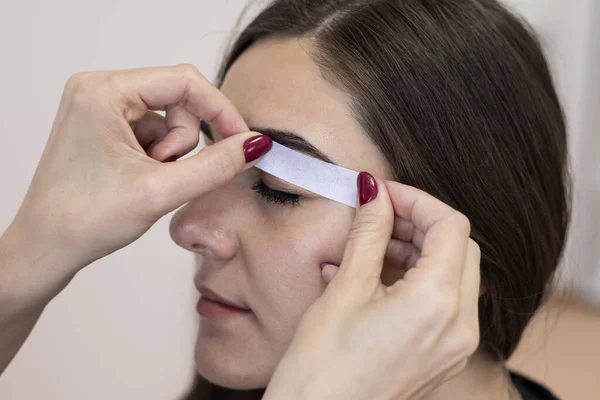 The master plucks wax strips or a paper shugaring bandage from the eyebrows, close-up. Waxing of the eyebrows.