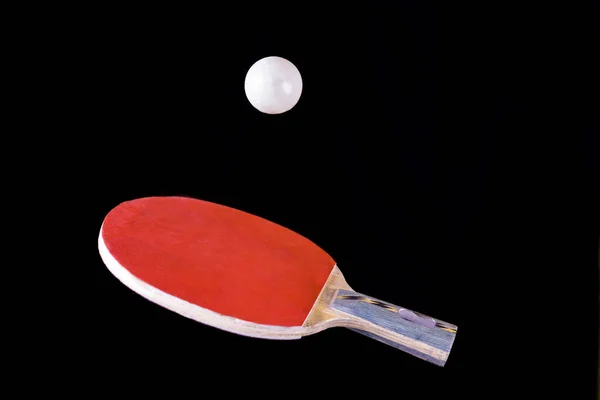 Red ping pong racket at the moment of throwing the ball. A red ping pong racket with a white ball on a black background. The concept of table tennis and ping pong.