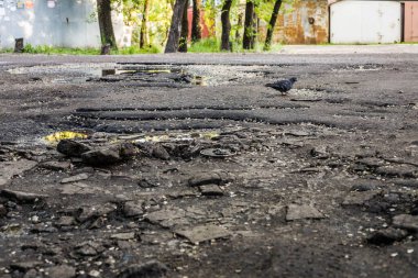 Çatlak ve tümseklerde delikler olan asfalt yollar yol kullanıcıları için tehlikelidir. Çukurlu asfalt kaldırım yolu hasar görmüş.