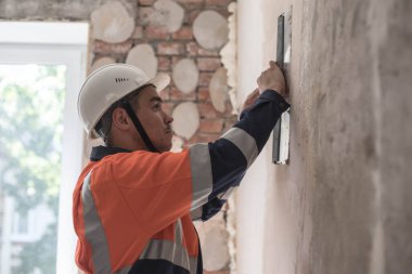 Sıkı şapkalı ve iş elbiseli bir adam bir apartman dairesinde tamirat yapıyor. Bitirme işi. Apartmanda profesyonel tamirat var. Sıva, boya, duvar onarımı.