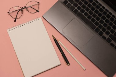 Üzerinde boş bir sayfa, gözlük, dizüstü bilgisayar ve ofis malzemeleri olan pembe bir defter. İş konsepti, evde çalışmak. Bağımsız.