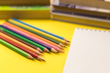 İçinde renkli kalemler ve sarı arka planda kitaplar olan boş bir not defteri. Bilgi Günü 'nde. Okula geri dön..