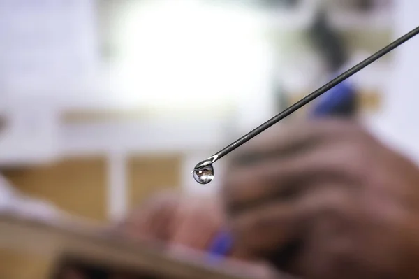 Syringe needle with a drop of serum on top. Blurred background that is reflected in the serum drop.