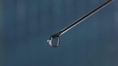 Üstünde bir damla serum olan şırınga iğnesi. Serum damlasına yansıyan bulanık arkaplan.