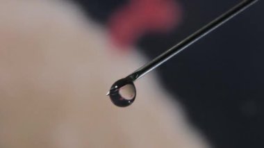 Üstünde bir damla serum olan şırınga iğnesi. Serum damlasına yansıyan bulanık arkaplan.