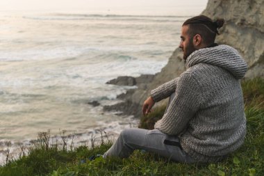 Denizin kenarındaki çayıra çam kozalağı atan bir adam.
