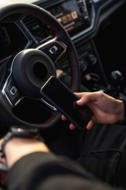 Tanımlanamayan bir adam pilot koltuğunda oturuyor, cep telefonu kullanıyor, koyu renk, modern kıyafetler giyiyor, bir elinde telefonu, diğer elinde akıllı bir saat var..