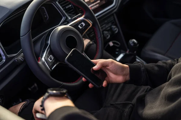 Tanımlanamayan bir adam pilot koltuğunda oturuyor, cep telefonu kullanıyor, koyu renk, modern kıyafetler giyiyor, bir elinde telefonu, diğer elinde akıllı bir saat var..