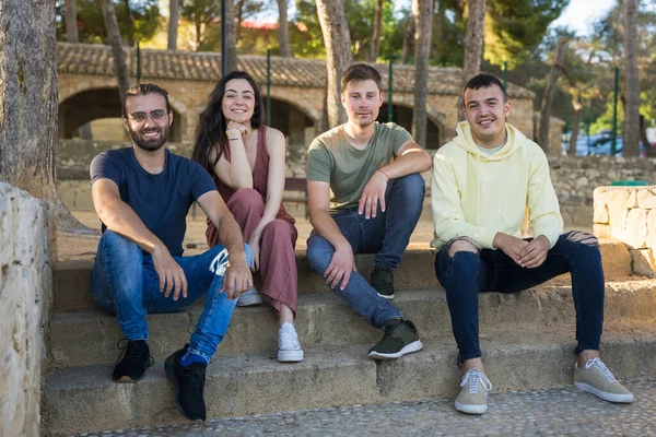Bir grup gülen arkadaş parkın merdivenlerinde oturuyor..