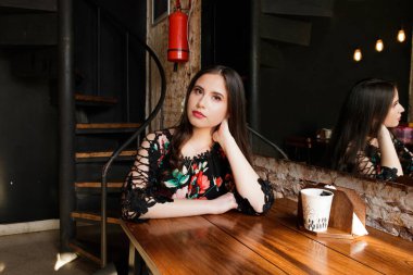 Koyu renkli bir ortamda beyaz tenli bir kız parlak lambalar, siyah duvar ve beton duvar, siyah kıyafetler ve çiçek detaylarıyla.