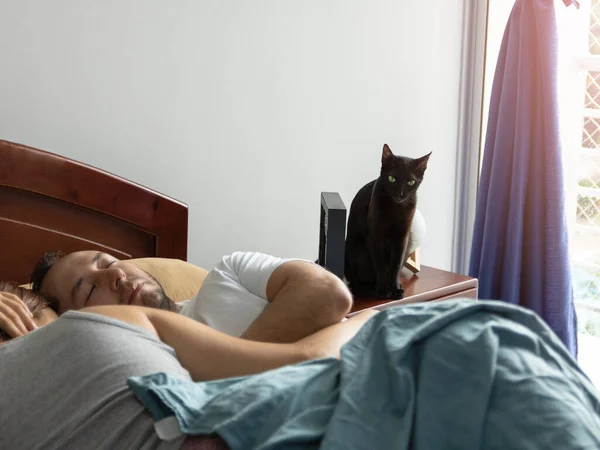 Yatakta uyuyan bir çiftin ve komodindeki bir kedinin stok fotoğrafı.
