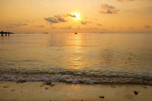 Seascape of beach during sunrise with silhouette of small boat Stock Image