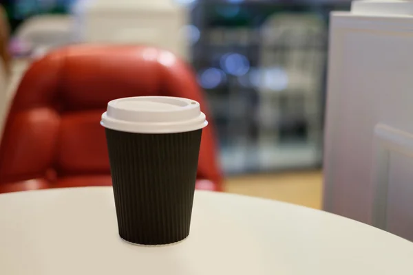 Paper cup of hot coffee with red chair background — Φωτογραφία Αρχείου