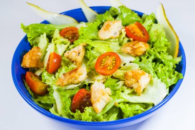 Yeşillikli tavuk salatası, domates ve elma mavi kasede.