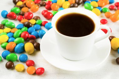 Beyaz arka planda bir fincan sade kahve ve çikolata şekeri renkli şeker dokusu