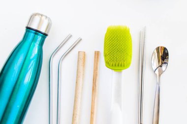 Düşük atık şeyler, su şişesi, bambu ve metal pipet, beyaz arka planda metal kaşık ve çubuklar.