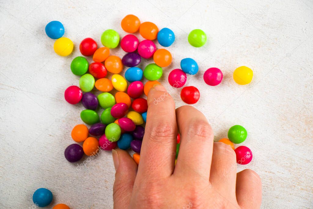Skittles candy in hand, colorful sweet candy background, high angle view