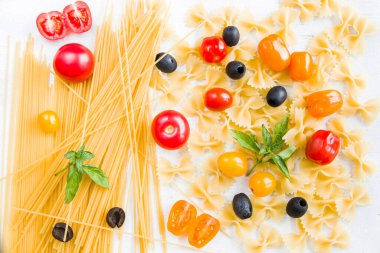 Beyaz arka planda makarna, çiğ makarna, kiraz domatesleri, zeytin ve fesleğen yaprakları.