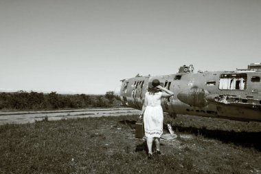 Kızıl şapkalı, güneş gözlüklü ve bavullu güzel kadınlar eski ve terk edilmiş Sovyetler Birliği jeti yakınlarında.