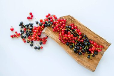 Ahşap ve beyaz arka planda kırmızı ve siyah frenk üzümü. Renkli meyveler.