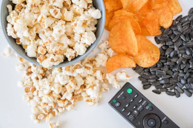 Beyaz arka planda kızarmış patlamış mısır ve televizyon kumandası.