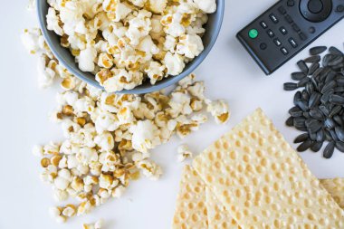 Beyaz arka planda kızarmış patlamış mısır ve televizyon kumandası.