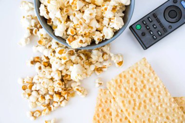 Beyaz arka planda kızarmış patlamış mısır ve televizyon kumandası.