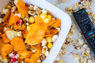 Beyaz arka plan ve televizyon kumandasında kızarmış patlamış mısır ve cips. Düşük açı.