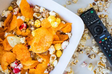 Beyaz arka plan ve televizyon kumandasında kızarmış patlamış mısır ve cips. Düşük açı.