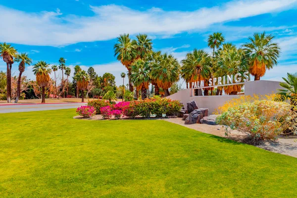 The Palm Springs sign stands at the landscaped entrance to Palm Springs. Bougainvillea and Palm trees surround the area in Southern California.