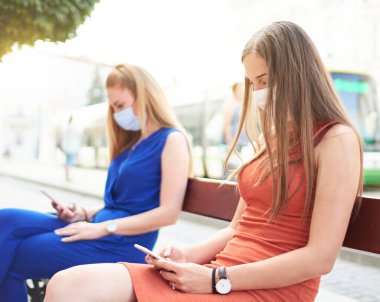 Akıllı telefonlar kullanan yüz maskeli kadın arkadaşlar - sosyal medya ağlarındaki güncellemeleri kontrol eden genç milenyum insanları - yeni normal