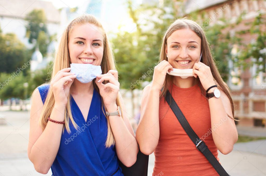 Young millennial friends with face mask after lockdown reopen - New normal friendship concept with girls having fun together