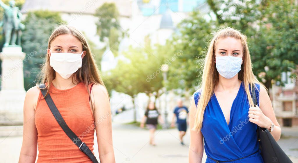 Woman friends walking with face mask after lockdown reopening - New normal friendship concept with girls spending time together on city streets - Social distancing