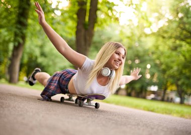 Genç, neşeli kaykaycı kız elleri havada bir yolda yuvarlanıyor, kulaklıklarla hayatın tadını çıkaran mutlu bir milenyum kadını, açık hava yaşam tarzı konsepti.
