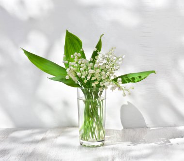 Beyaz çiçekli vadideki Zambak (Convallaria majalis, Mayıs çanları, mayıs zambağı) beyaz bir masada yazı için yer var.