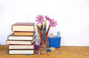 Okula geri dön. Okul gereçleri (kitap, kalem, bileyici, ataçlar, pembe çiçekler) açık arkaplan üzerindeki ahşap masa üzerinde