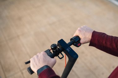 Elleri düğmelere değen elektrikli paten. Şehirde dolaşmak için elektrikli paten kullanan genç bir adam..