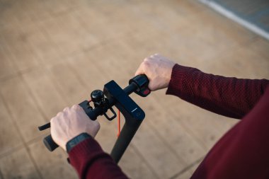 Elleri düğmelere değen elektrikli paten. Şehirde dolaşmak için elektrikli paten kullanan genç bir adam..