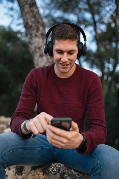 Boy listening to music with wireless headphones and using his cell phone. Red vest.
