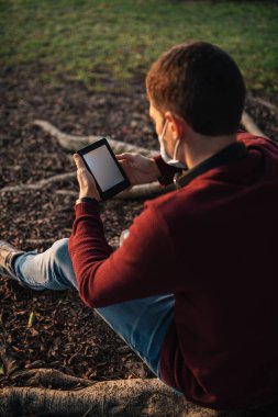 Covid-19 'un yanındaki maskeli çocuk e-kitap okuyor, gün batımında ağaçta oturuyor..