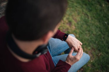 Akıllı saati olan, kalp atışlarını ölçen bir adam. Kalp akıllı saat ekranında. Sağlıklı yaşam kavramı. Çimenlerde otururken.