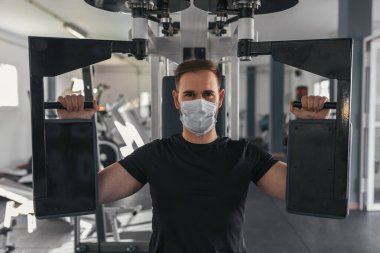 Genç adam maske takan bir jimnastik makinesi kullanıyor. Spor ve sağlık konsepti.