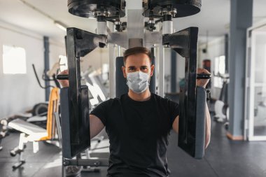 Genç adam maske takan bir jimnastik makinesi kullanıyor. Spor ve sağlık konsepti.