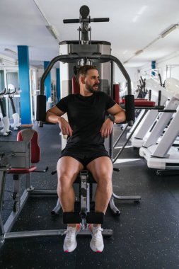Genç adam spor salonunda bir makinenin üzerinde yan tarafa bakıyor. Ona odaklan. Sağlık ve refah kavramı.