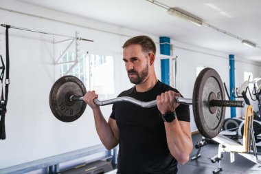 Bisepsli kıvırcık saçlı genç bir adam. Bar egzersizi. Sağlık ve refah kavramı