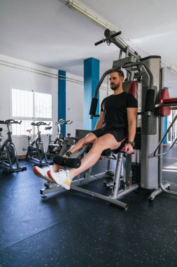 Spor salonunda bacak egzersizi yapan yakışıklı bir adam. Ona odaklan. Dikey